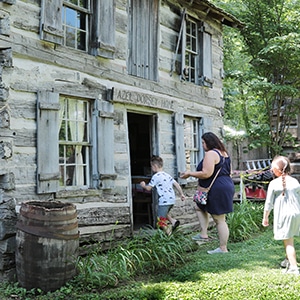 Mom and two kids entering a log cabin at Lincoln Pioneer Village & Museum